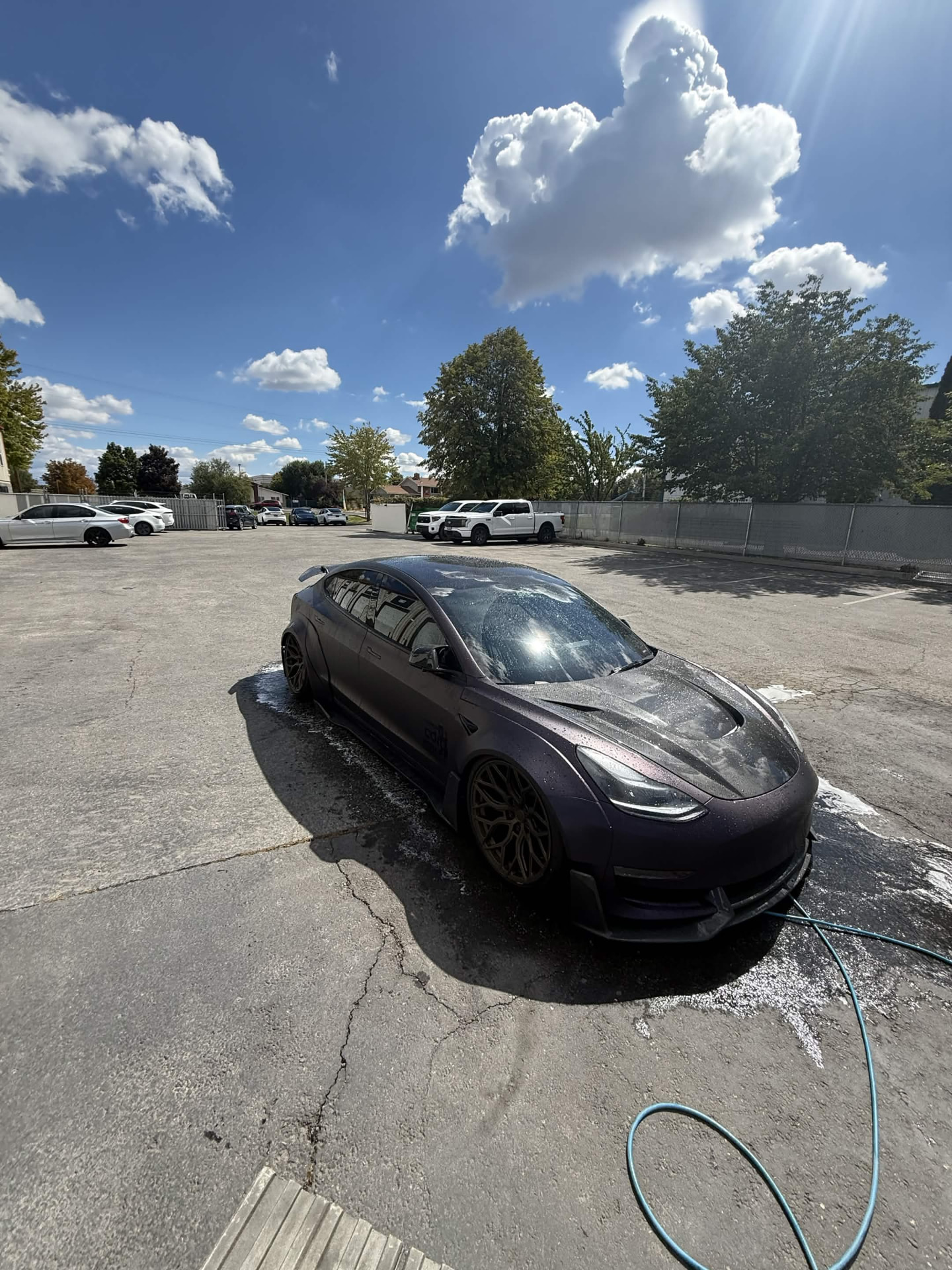 Matte plum Tesla Model 3 widebody with a carbon-fiber hood being rinsed with foam in a parking lot
