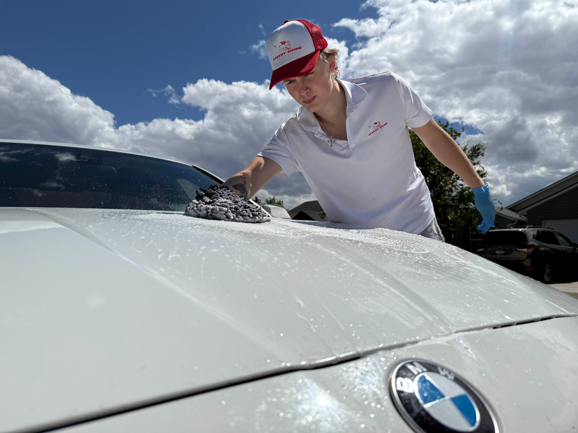 Speedy Shine detailer hand washing the hood of a white BMW